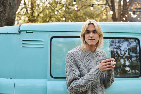 A young and handsome man stands thoughtfully by a vintage van surrounded by nature.
