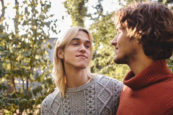 Two handsome young men share a heartfelt glance in a lush garden filled with greenery. They radiate joy and companionship, enjoying a beautiful day outdoors, surrounded by nature and warmth.
