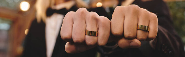 Two young men proudly show off their matching rings, symbolizing their love and commitment. Friends and family surround them, creating a joyful atmosphere filled with laughter and celebration.