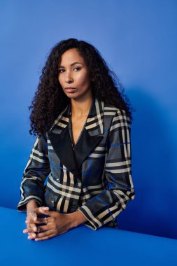 Göz kamaştırıcı bir kadın, zarif bir pozla, mavi bir arka plana vurgu yapar..