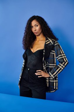 Göz kamaştırıcı bir kadın kendine has tarzını sergilerken canlı bir mavi arkaplana karşı duruyor..