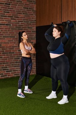 Two women engaged in a focused workout, showcasing strength and encouragement in the gym. clipart