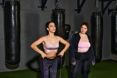 İki kadın spor salonundaki antrenman rutinlerine odaklanır, fitness ve takım çalışmasını desteklerler..