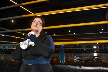 Kadın biraz soluklanıyor, hareketli bir spor salonunda eğitim yolculuğunu yansıtıyor..
