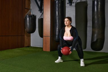 Odaklanmış kadın, şık bir spor salonunda, yanında kum torbalarıyla ağır bir egzersiz yapıyor.
