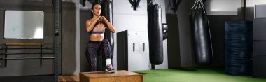 Kendini işine adamış bir kadın spor aletleriyle çevrili sağlam bir kutuda egzersiz yapıyor..