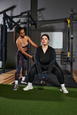 Trainer provides support to beginner as she lifts weights in a well equipped fitness center. clipart