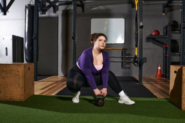 Kettlebell ile egzersiz yapan, kendini adamış bir kadın şık bir spor salonunda spor yapmayı benimser..
