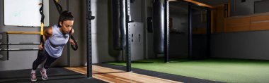 Kadın antrenman sırasında iyi donanımlı bir spor salonunda süspansiyon şınav çekiyor..