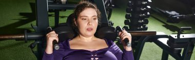 Odaklanmış bir kadın, iyi aydınlatılmış bir spor salonunda ekipmanla güç eğitimi alıyor..