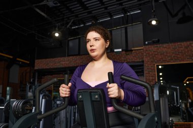 Odaklanmış kadın tutkulu bir idmana girişiyor, hareketli bir spor salonunda sınırları zorluyor..