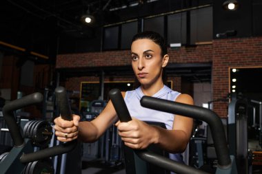 Kendini adamış bir kadın modern bir spor salonunda yoğun bir şekilde egzersiz yapıyor, fitness hedefleri için çabalıyor..