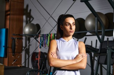 Bir kadın kendinden emin bir şekilde kollarını kavuşturup spor salonunda bağlılığını ve konsantrasyonunu gösterir..