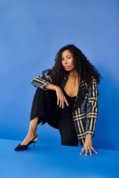 A confident woman showcases her fashion sense against a bold blue backdrop.