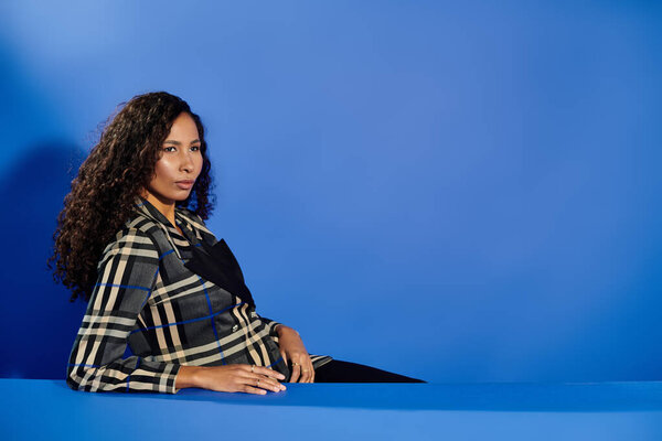 A stunning woman in a stylish outfit showcases her confidence in a captivating blue setting.