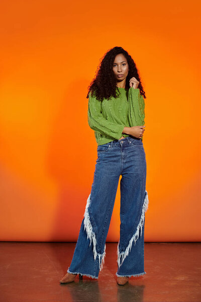 Уверенная женщина оглушает в зеленый свитер и модные широкие джинсы для ног.