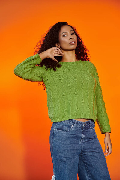 Красивая женщина уверенно позирует, демонстрируя свой стильный зеленый свитер жирными цветами.