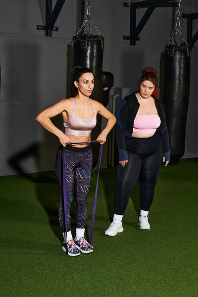 Женщины выполняют упражнения с бандами сопротивления в хорошо оборудованном тренажерном зале во время тренировки.