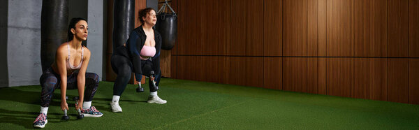 Две преданные женщины выполняют приседания с гирями в стильной обстановке спортзала.