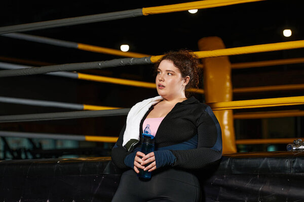 Посвящённая женщина отдыхает и заправляется водой после энергичной тренировки в спортзале.