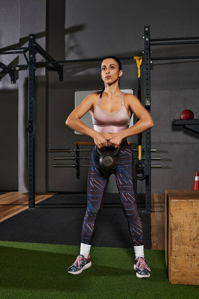 Dedicated woman performs kettlebell exercise in a modern gym environment with equipment.