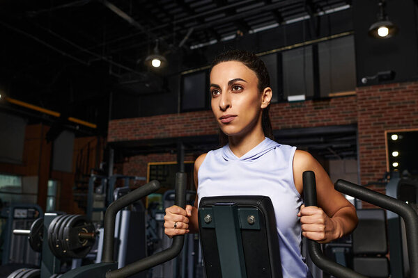 Dedicated woman works on upper body strength using gym equipment in an energetic environment.