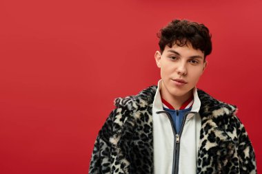 Yakışıklı bir adam gösterişli bir leopar desenli ceket sergiliyor, koyu kırmızı bir fonda duruyor..
