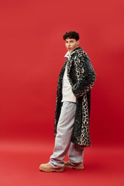 Kendine güvenen bir adam dikkat çekici kırmızı arkaplanlı leopar desenli bir ceketle eşsiz bir moda sergiliyor..