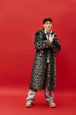 Cesur bir leopar desenli ceket giymiş yakışıklı bir adam dikkat çekici bir kırmızı ayar içinde duruyor..