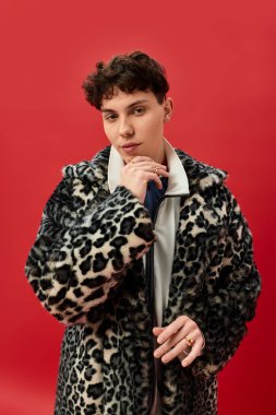 Leopar desenli ceketli şık bir adam kırmızı bir zemine sert bir şekilde poz veriyor..