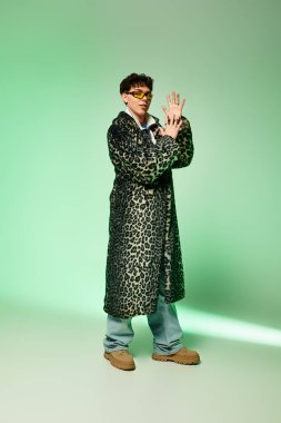 A stylish man stands confidently in a vibrant studio, wearing a leopard coat and trendy shades. clipart