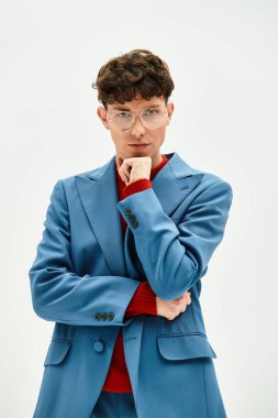 Mavi takım elbiseli ve gözlüklü yakışıklı adam minimalist bir ortamda düşünceli bir poz veriyor..