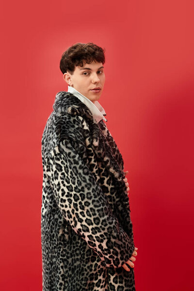 Человек надевает яркое леопардовое пальто, демонстрируя уникальный стиль на яркой красной стене.