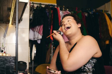 Kendine güvenen bir travesti, canlı bir soyunma odasında neşeli bir etkinliğe hazırlanmak için makyaj yapar..