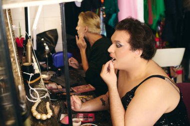 Bir travesti, bir tatil gösterisinden önce canlı bir kulis odasında cesur bir makyaj yapar..