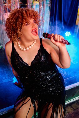 Aşırı makyajlı enerjik travesti şenlikli bir etkinlikte tutkuyla performans sergiler.