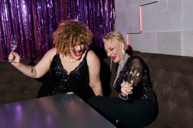 Abartılı makyajlı iki travesti yeni yıl kutlamalarında şampanya içiyor.