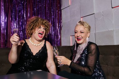 Abartılı makyajlı heyecanlı travestiler yeni yıl kutlamalarında şampanya içiyorlar.