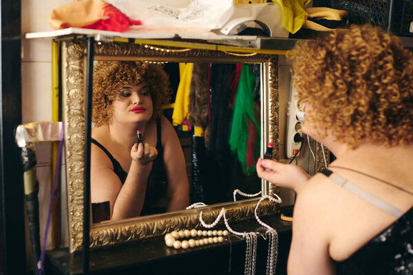 Colorful preparations unfold in a backstage dressing room as a drag queen applies makeup.