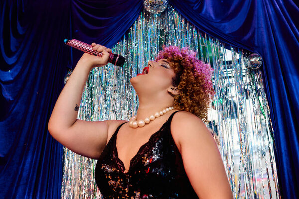 Опытная королева дрэг-рейсинга танцует с ярким макияжем и стилем в живом выступлении на сцене.