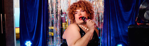 Дерзко украшенный ярким макияжем, трансвестит светит на сцене во время праздничного шоу.