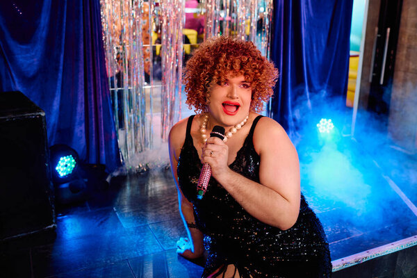 Дерзко украшенный ярким макияжем трансвестит аудиторию во время праздничного шоу.