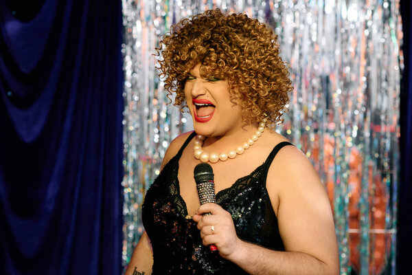 A drag queen with bold makeup puts on a lively holiday show, captivating the audience.