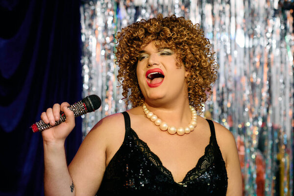 Экстравагантный трансвестит очаровывает толпу потрясающим макияжем и мощным вокалом на сцене..