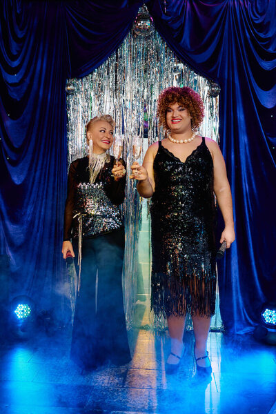 Эксцентричные трансвеститы сияют на сцене, ослепляя толпу своим экстравагантным праздничным шоу.