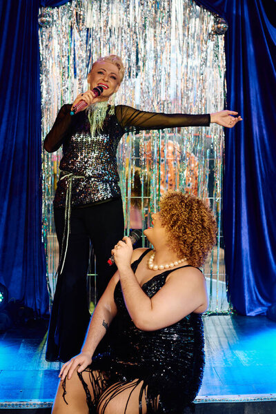 Два ярких трансвестита исполняют очаровательный дуэт на сцене, одетые в экстравагантные наряды.