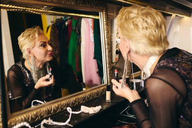 Bir travesti titizlikle soyunma odasına makyaj yapar, tatil şovu için hazırdır..