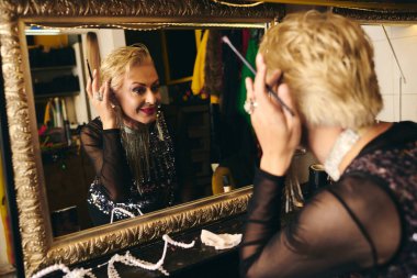Çift cinsiyetli bir travesti sahne arkası soyunma odasında makyaj yapar, heyecanı yansıtır..