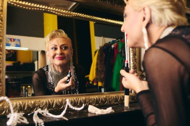 Canlı bir soyunma odasında, bir travesti dikkatlice bir tatil programı için makyaj yapar..