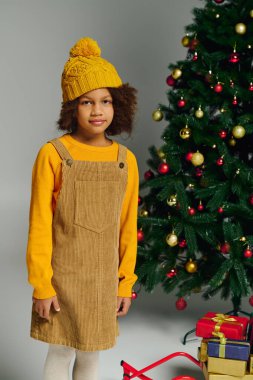Genç kız neşeli bir kıyafet giyer ve hediyelerle çevrili bir Noel ağacının yanında durur..